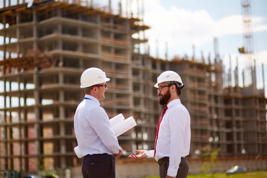 Small group of businessmen in helmets and formalwear talking in front of unfinished construction