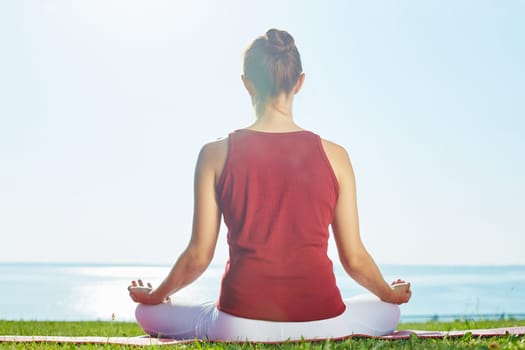 Back of young woman meditating by the seaside