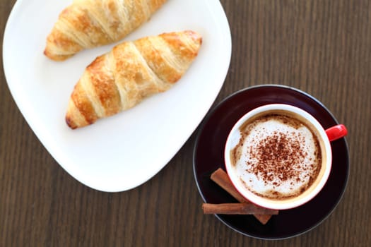 An italian cappuccino served with cocoa and croissant with intentional blurred background