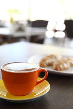 An italian cappuccino served with cocoa and croissant with intentional blurred background