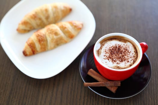 An italian cappuccino served with cocoa and croissant with intentional blurred background