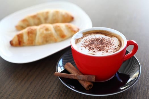 An italian cappuccino served with cocoa and croissant with intentional blurred background