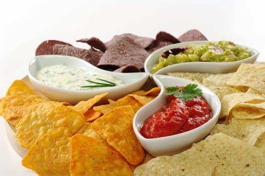 Three different dips (guacamole, tomato-chili and cream cheese dip) with salty and cheese tacos and chips made of Peruvian purple corn on white (Selective Focus)