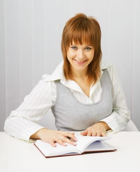 Attractive girl in a white blouse with a notepad and pen on the background of blinds.