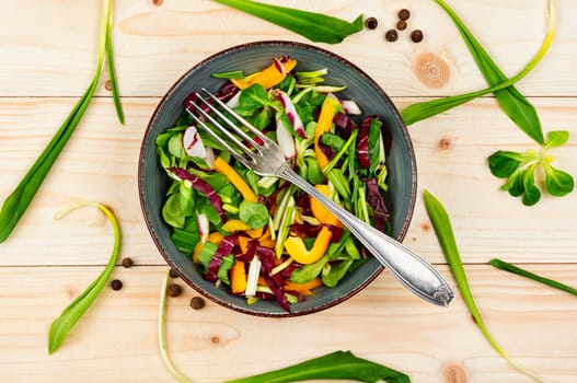 Healthy salad with vegetables and leaves of wild garlic on a rustic wooden board.