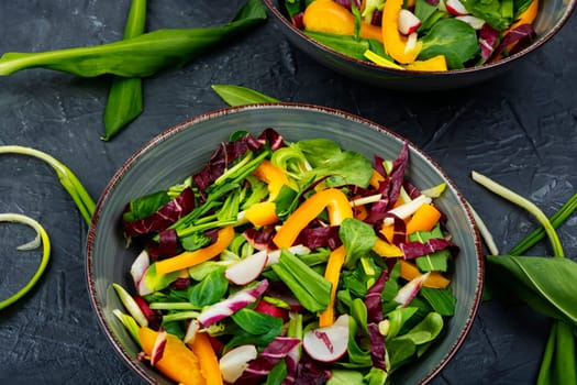 Healthy salad with vegetables and leaves of wild garlic on a rustic wooden board.
