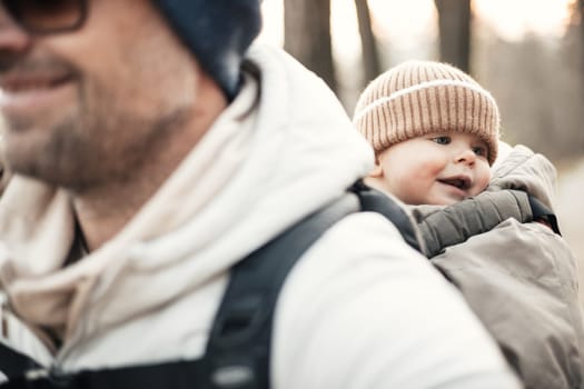 Sporty father carrying his infant son wearing winter jumpsuit and cap in backpack carrier hiking in autumn forest