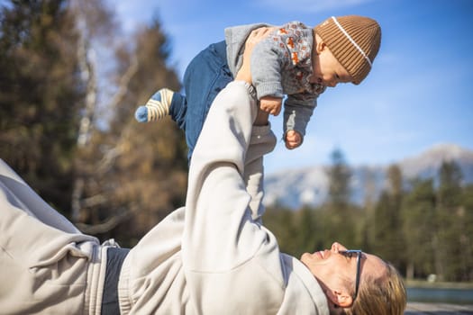 Happy family. Young mother playing with her baby boy infant oudoors on sunny autumn day. Portrait of mom and little son on wooden platform by lake. Positive human emotions, feelings, joy