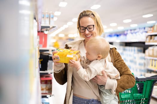 Caucasian mother shopping with her infant baby boy child choosing products in department of supermarket grocery store