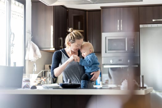 Happy mother and little infant baby boy making pancakes for breakfast together in domestic kitchen. Family, lifestyle, domestic life, food, healthy eating and people concept
