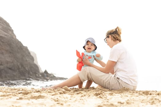 Mother playing his infant baby boy son on sandy beach enjoying summer vacationson on Lanzarote island, Spain. Family travel and vacations concept
