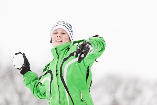 Young boy enjoying the cold winter weather smiling happily as he prepares to throw a snowball during a snowball fight, upper body portrait in a winter landscape