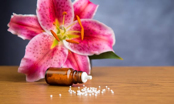 homeopathic globules on wooden ground with lilly blossom