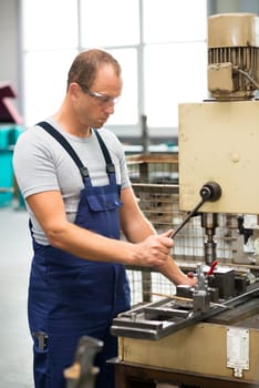 young worker in factory on drilling machine