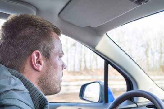 Young man drives a car,holds his right hand on the steering wheel.