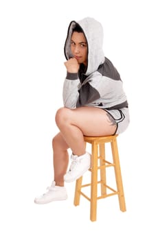 A lovely young woman in a gray hoodie and shorts sitting on a chair,.with her hand on her chin, isolated for white background..
