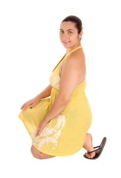 A lovely young woman in a yellow dress and sandals, kneeling on the.floor, isolated for white background..