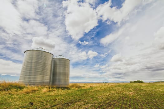 Metal grain silos on a prairie landscape with a blue cloudy sky.