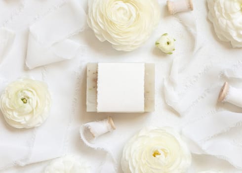 Handmade soap bar with blank label near cream roses and white ribbons top view, soap mockup. Beauty product for face and body care. Natural Spa cosmetic concept