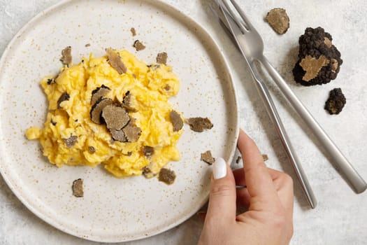 Hand with plate with Scrambled eggs with fresh black truffles top view. Italian cousine, gourmet breakfast