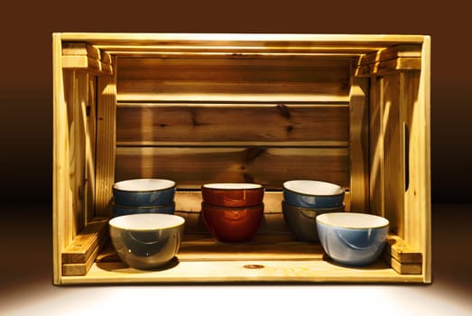 Several ceramic bowls stand very decoratively in a wooden box.