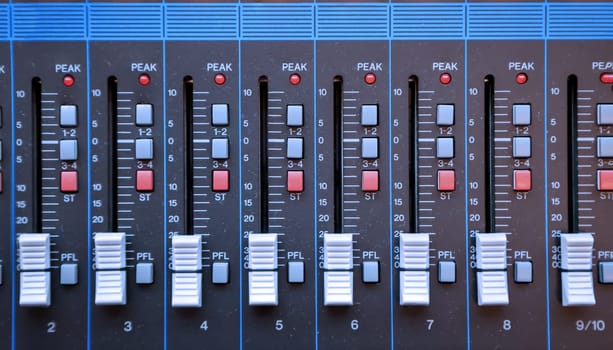 A detailed view of a DJ's mixing desk, knobs and sliders.