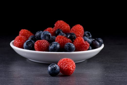Plate of fresh blueberries and raspberries on balck background