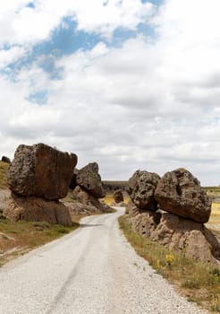 precarious balanced volcanic rocks on either side of a public dirt track, Cappadocia, Turkey. Volcanic terrian, lava rock, limestone, sandstone, blue cloud layered sky, portrait, copy space, crop area, scenic