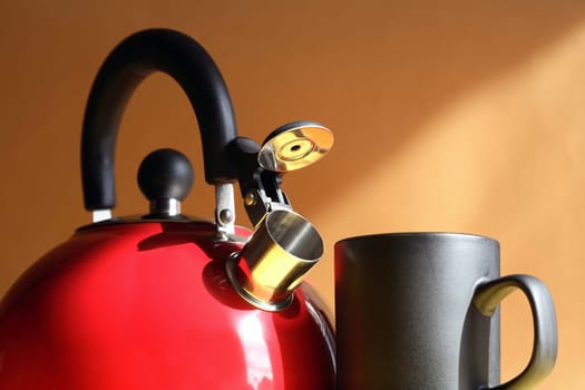Closeup of red metal kettle near black mug on background with sunbeam