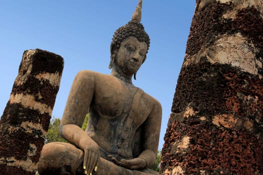 large seated buddha with gold leaf on fingernails in sukhothai historical park temple ruins in northern thailand