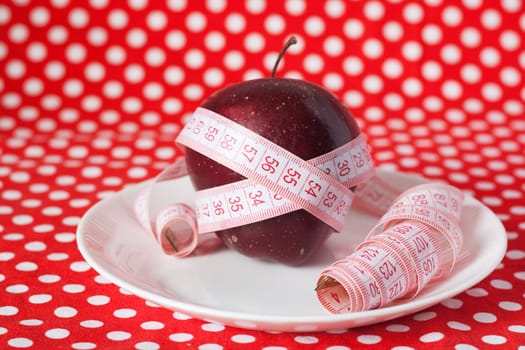 Red apple and measuring tape on a white plate