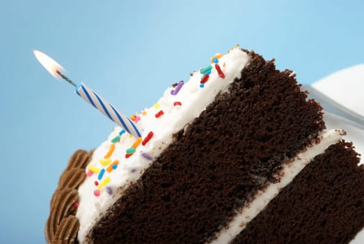 A slice of chocolate cake with a single lit candle.