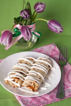 Pancakes with sour cream for breakfast and a vase of purple tulips