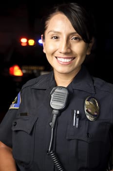 a female police officer smiling at night with her patrol car in the background.