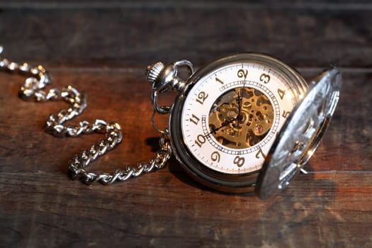Vintage pocket watch with open lid and chain on wooden surface