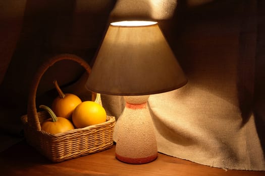 Basket with three pumpkins near luminous desk lamp on canvas background
