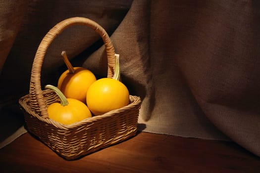 Woven basket with three pumpkins on dark canvas background