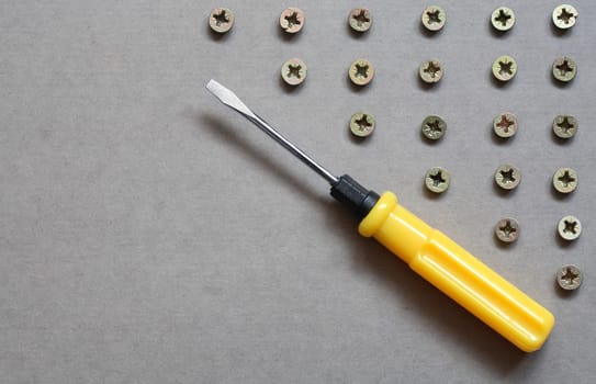 Industrial concept. Yellow screwdriver near lot of screws on gray surface with copy space