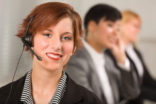Pretty Red Haired Businesswoman with Headset and Colleagues Behind in Office Setting.