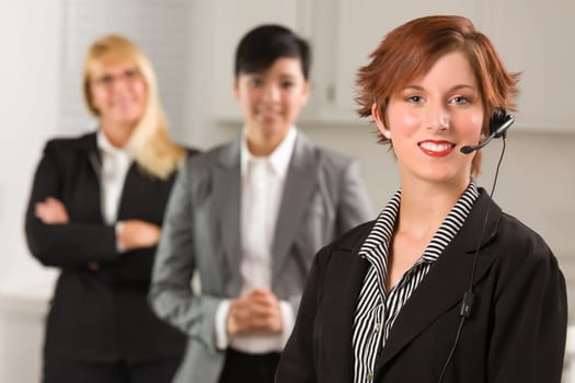Pretty Red Haired Businesswoman with Headset and Colleagues Behind in Office Setting.