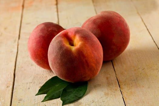 photo of delicious peaches on wooden table with leaves