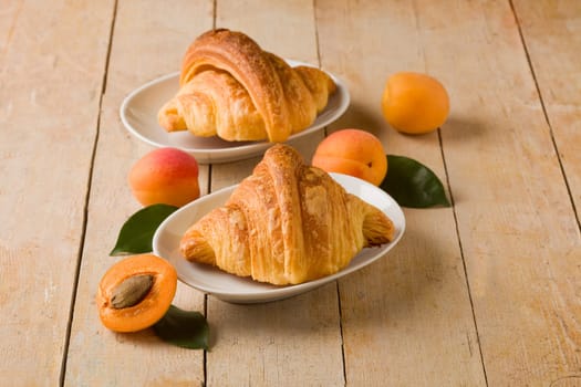 photo of delicious golden croissants with apricot marmalade on wooden table