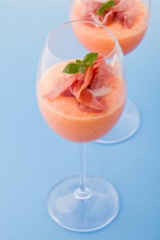 photo of delicious ham and melon cocktail appetizer on light blue background