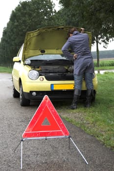 Pretty brunette bend over the insides of her car (focus on the girl) with danger triangle in front