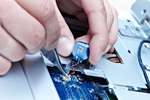 macro of hands with tweezers disconnecting a laptop battery