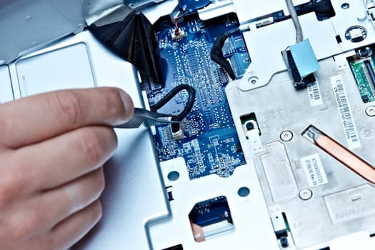 macro of a hand holding tweezers on a laptop connector