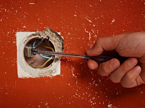 close up of hand holding a screwdriver in front of a electrical wall socket