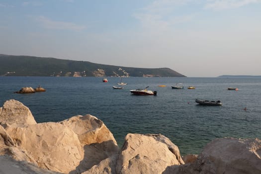 Herceg Novi, Montenegro 08.09.2022 Sea vacation trip. Boats float on Adriatic Sea. Mediterranean travel business. Sailboats and mountains. Small ripples on salt water. Sunny weather. Stones and rocks