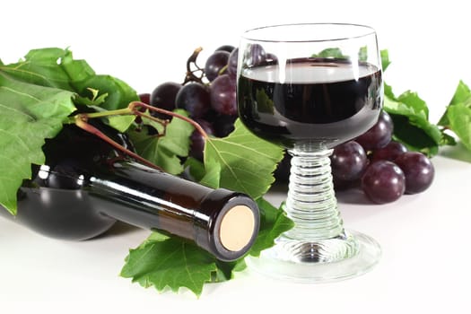 a bottle of red wine with glass, grapes and vine tendril on a white background