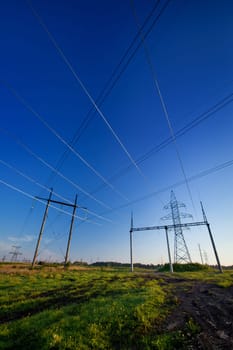 Electric power lines in a field over blue morning sky with many crossing wires. Vertical